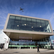 Photo de l'extérieur du centre commercial d'aéroville avec un avion qui passe au dessus dans le ciel bleu