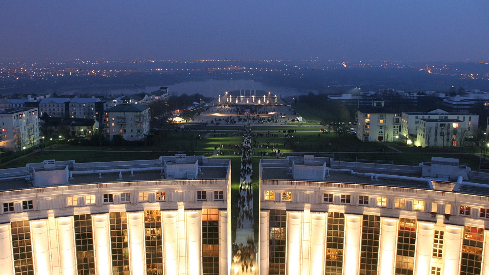 Photo prise depuis la Tour du Belvédère, la nuit tombante. Événement, festival ou concert sur l'esplanade de Paris de Cergy Saint-Christophe. Vue sur l'Île de loisirs, les Étangs de Cergy et les lumières de Paris.