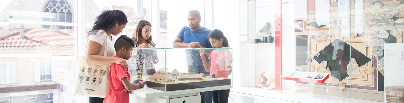 Photo d'une famille au musée Archéa à Louvres avec une guide de musée qui explique ce qu'il y a en vitrine