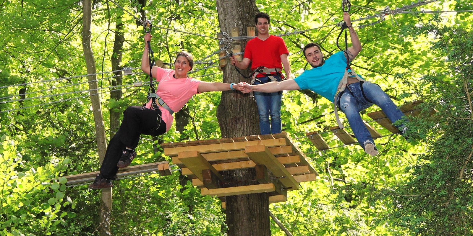 Photo d'un couple se tenant la main au milieu des arbres pendant qu'ils descendent une tyrolienne d'un parcours d'accrobranche au parc Aventure Land à Magny en Vexin dans le Val d'Oise