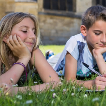 Photo de deux enfants dessinant sur un carnet de visite allongés dans l'herbe devant l'église d'Auvers sur Oise dans le Val d'Oise