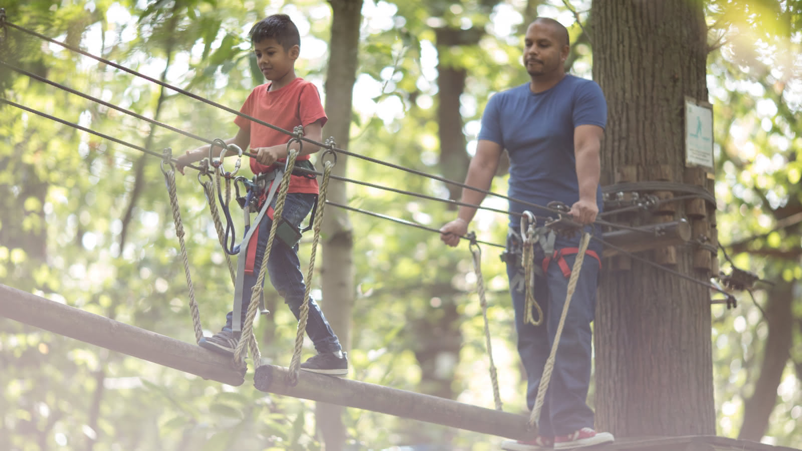 Photo d'un jeune garçon au t shirt rouge avec son papa sur un parcours d'accrobranche au parc Sherwood Parc dans le Val d'Oise
