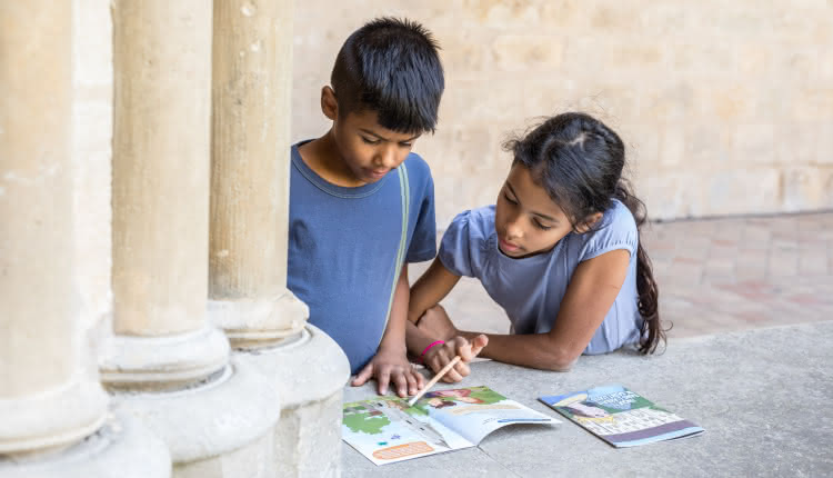 Photo d'une petite fille avec son frère en train de lire les carnets de visite pour enfant sous les voûtes du cloître