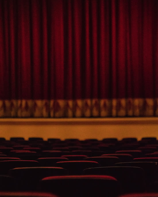 Photo d'une salle de spectacle vide avec des siège et un rideau rouge.