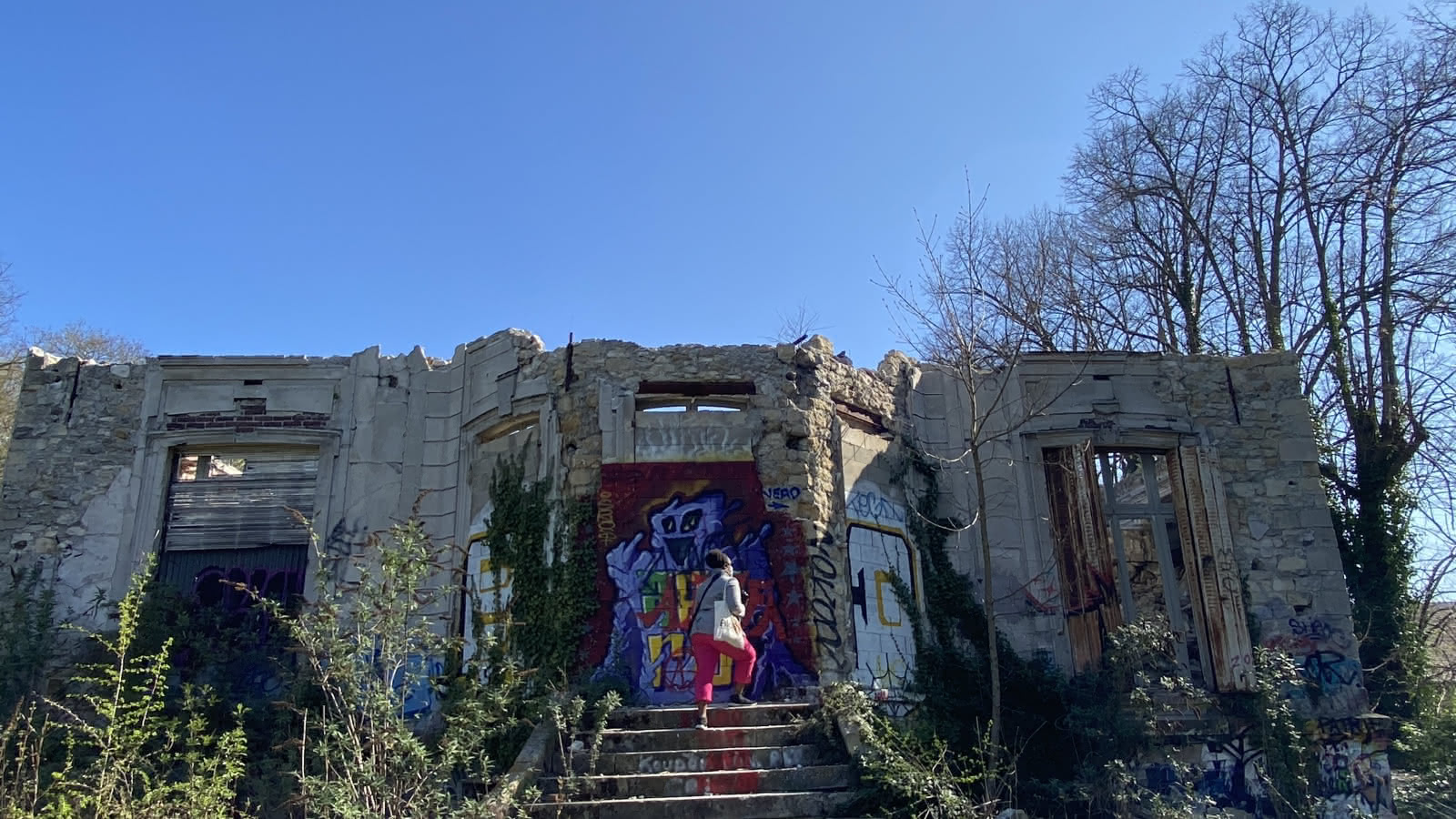 Femme de dos, montant les marches d'une ruine dont la façade est recouverte de graffitis à Goussainville