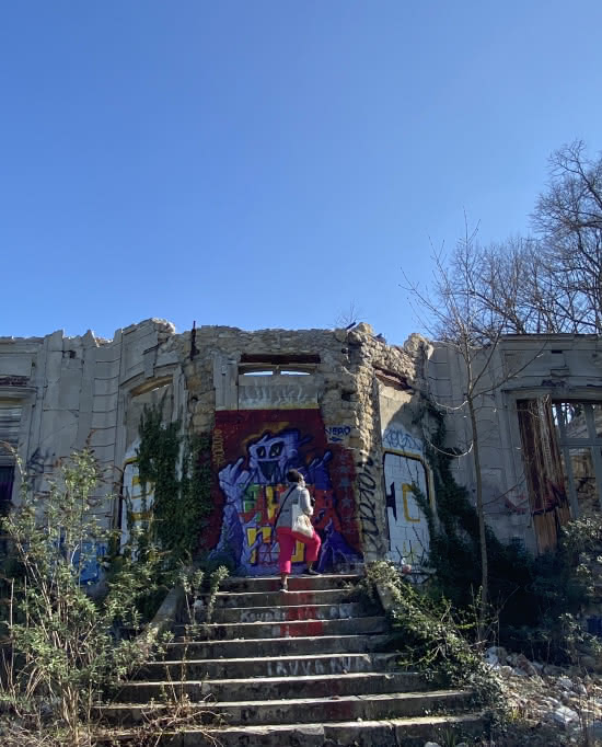Femme de dos, montant les marches d'une ruine dont la façade est recouverte de graffitis à Goussainville