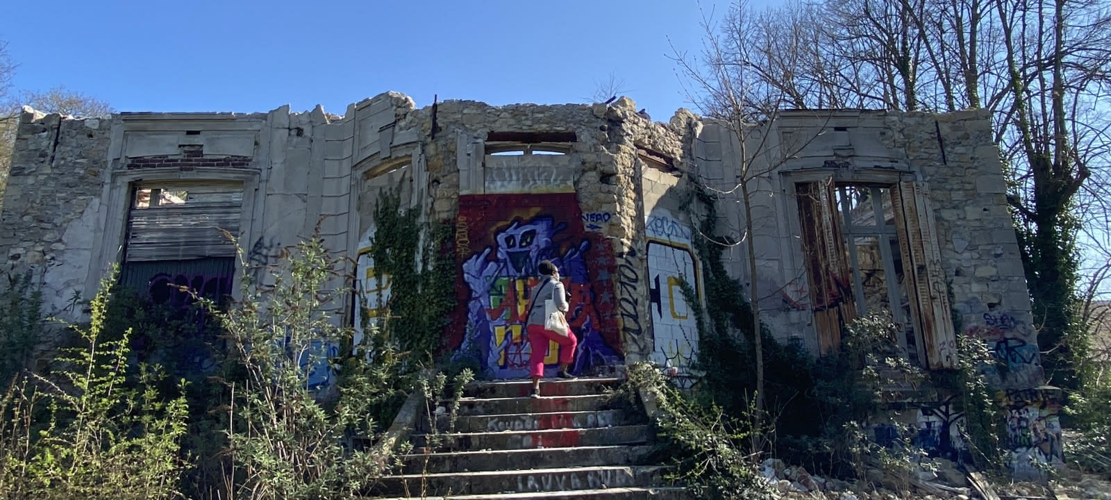 Femme de dos, montant les marches d'une ruine dont la façade est recouverte de graffitis à Goussainville